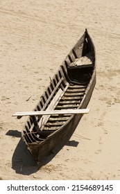 A Wooden Rowing Boat Sits On The Sand Alone With A Plank Across It, All Forming A Shadow