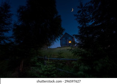 Wooden rural house on the green hill between of big carpathian spruce trees at twilight hour. New moon over it.