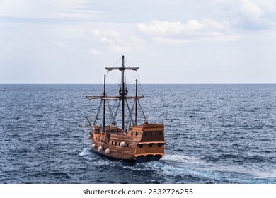 A wooden sailing ship moving through a calm sea under a partly cloudy sky. The ship appears to be an old-fashioned or historical vessel, reminiscent of pirate ships or early exploration vessels.  - Powered by Shutterstock