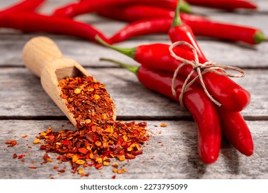 Wooden scoop with crushed chili pepper and fresh red chili pepper on old table. Selective focus. - Shutterstock ID 2273795099