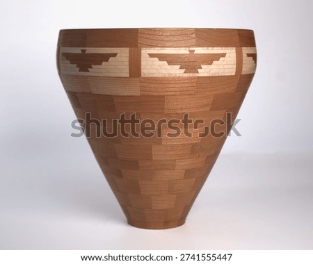 A wooden segmented vessel with a Thunderbird pattern. The vessel is V shaped and handcrafted by a woodworking artisan. 