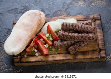 Wooden serving tray with grilled balkan cevapi, pitas, tomatoes and onion, studio shot
