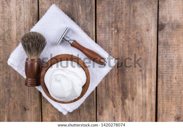 \
Wooden shaving razor with shaving brush and\
shaving foam on a rustic wooden table - vintage shaving accessories\
- top view