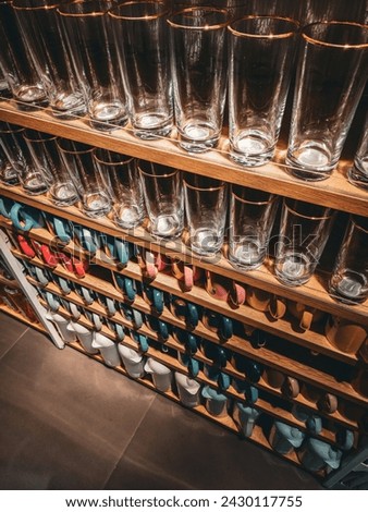 A Wooden shelf mounted on a white wall. The shelf is filled with a variety of glasses and mugs.