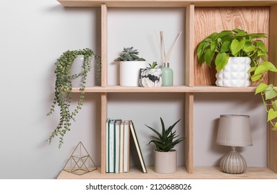 Wooden shelving unit with interior accessories and houseplants on white wall - Shutterstock ID 2120688026