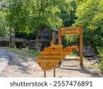 A wooden “Almost Heaven” sign welcomes visitors to the historic Glade Creek Grist Mill in Babcock State Forest, West Virginia, surrounded by lush greenery.