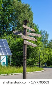 Wooden signpost with wooden arrows on the background of green trees, blue sky and solar panels