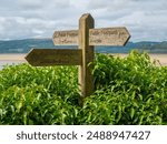 Wooden signpost with footpath directions Arnside Cumbria amidst lush greenery, with scenic landscape in the background.