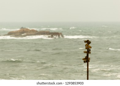 Wooden signpost with many pointers with the sea at background.