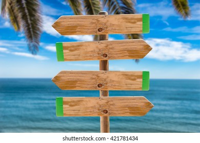wooden signpost in the meadow with copyspace on the ocean and palms background