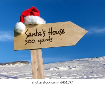 Wooden signpost with Santa's hat indicating Santa's House with snow and blue sky in the background - Shutterstock ID 6451597