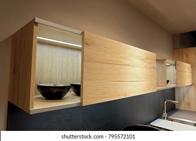 Wooden Sliding Door Wall Cabinet And Black Bowls Inside With Lighting In Kitchen Room.