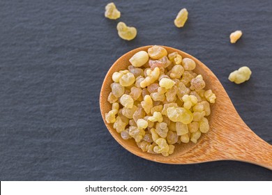 Wooden spoon of Aromatic yellow resin gum from Sudanese Frankincense tree, incense made by slashing bark of Boswellia sacra tree in Etiopia on dark black stone background