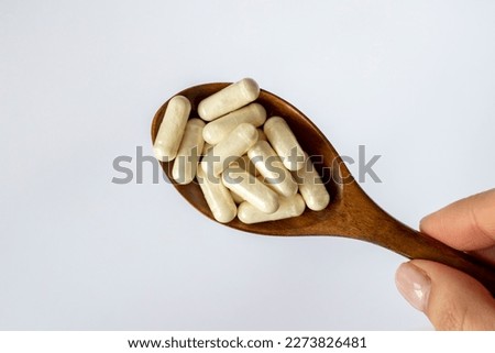 Wooden spoon with beige capsules in a woman's hand on a white background. Close-up, top view. Pills, vitamins, minerals, supplements or enzymes.