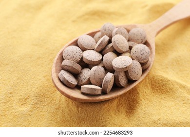 Wooden spoon of brewer`s yeast tablets on powder, closeup