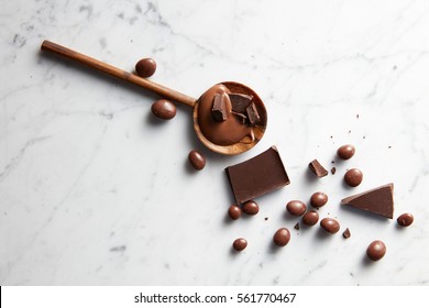 wooden spoon with caramel, chocolate chips and chocolate balls on white marble background