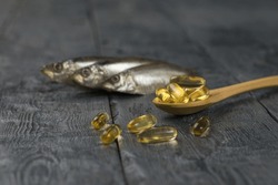 Wooden Spoon With Fish Oil Capsules On The Background Of Three Fish On A Wooden Table. Biologically Active Additive.
