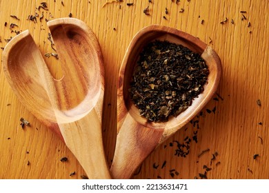 Wooden Spoon And Fork On The Kitchen Table With Scattered Green Tea Leaves. Modern Warm Kitchen Backdrop