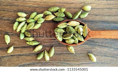 Wooden spoon full of asian green spice dry cardamom on textile background. Aromatic flovour seeds for healthy organic food. Asia spicy plant for cooking, medicine, ayurvedic treatment. Closeup.