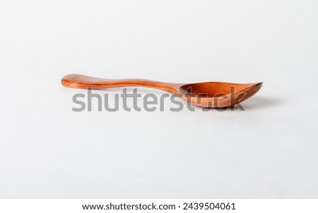 A wooden spoon is sitting on a white table. The spoon is long and thin, with a curved end. The spoon is made of wood and has a natural, rustic appearance. Concept of simplicity and warmth