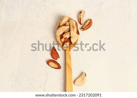 Wooden spoon with tasty Brazil nuts on light background