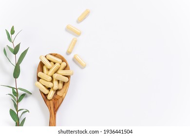 Wooden spoon with vegan vitamin capsules for immunity support and healthy lifestyle on white background with fresh green eucalyptus twig.