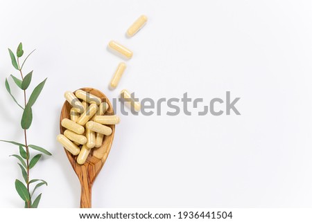 Wooden spoon with vegan vitamin capsules for immunity support and healthy lifestyle on white background with fresh green eucalyptus twig.
