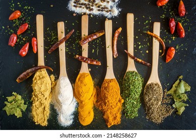 Wooden spoons filled with spices, curry, ginger, paprika, parsley, thyme, salt, on a black background.