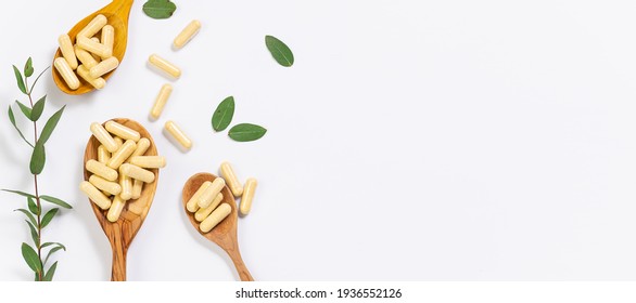 Wooden spoons with vegan vitamin capsules for immunity support and healthy lifestyle on white background with fresh green eucalyptus twig. Long banner format.