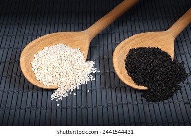 wooden spoons with white and black sesame seeds on a dark bamboo mat background