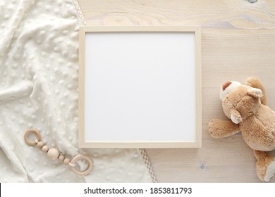 Wooden square frame mockup, empty frame mock up for nursery, baby room artwork, photo, sayings, flat lay composition with baby blanket, teddy bear and baby teether.     - Shutterstock ID 1853811793