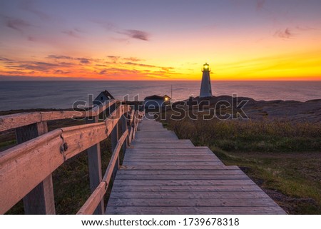 Wooden staircase and boardwalk at a beautiful sunrise, overlooking a white lighthouse sitting at the edge of a rocky cliff.  Cape Spear National Historic Site, St Johns Newfoundland. 