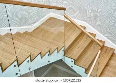 Wooden staircase with glass railings and wooden handrail. View from above