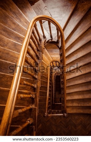 Wooden staircase - view from above. Perspective view of clockwise U-shaped staircase in an old house. Orange-brown-ish stairs and handrails made of wood.