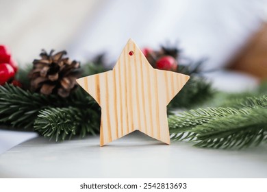 A wooden star ornament rests on a table, surrounded by pinecones and lush evergreen branches, adding a festive touch to the holiday decor during the winter season. - Powered by Shutterstock