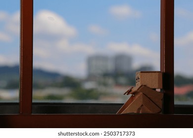 A wooden statue with a depressed emoji face sits on a window railing looking out against a blurred landscape. - Powered by Shutterstock