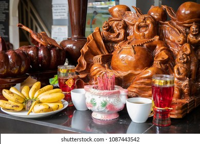 Wooden statue of laughing Buddha with scented stick and food gift. Asian religious belief. Buddhist shrine indoor. Buddhist home decor. Wealth and prosperity symbol. Offering to happy Buddha fat belly