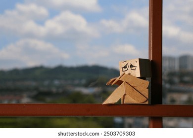 A wooden statue with a sad face by the window with a blurred landscape background. - Powered by Shutterstock