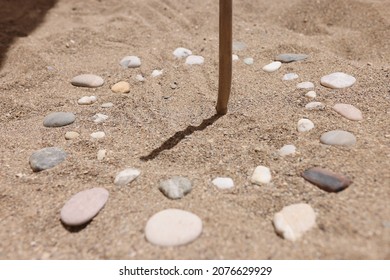 Wooden stick and pebbles on sand showing time by shadow - Powered by Shutterstock