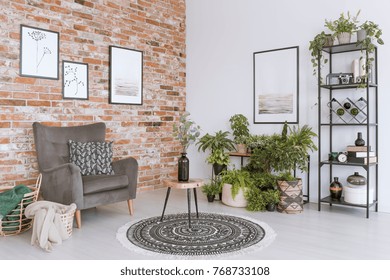 Wooden stool with vase on round patterned carpet in relax room with grey armchair against brick wall