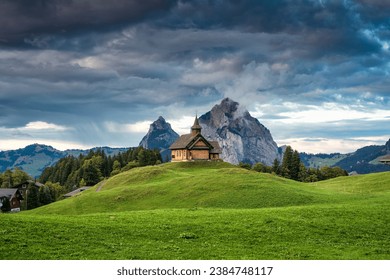 Wooden Stoos church on green hill in front of Grosser Mythen mountain in summer at canton of Schwyz, Switzerland