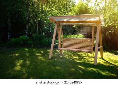 Wooden summer swing on the green grass in the garden. Garden decoration. Landscape design.Summer vacation in the country.