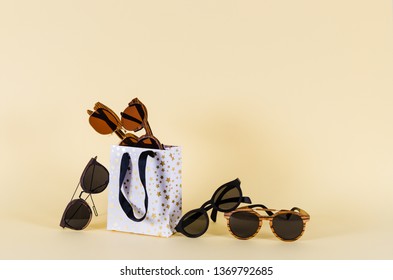 Wooden sunglasses of different design in shopping bag on yellow background. Sunglasses sale concept. Fashion summer accessories.