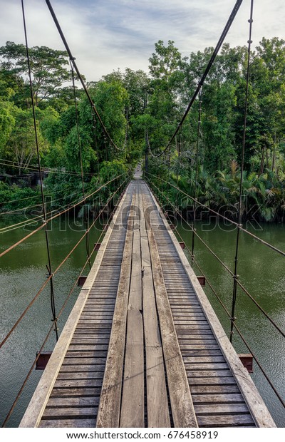 Wooden\
suspension bridge across the canal Sawi district of Chumphon Bamboo\
and trees from both sides. The wooden\
bridge