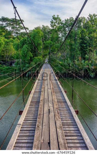 Wooden\
suspension bridge across the canal Sawi district of Chumphon Bamboo\
and trees from both sides. The wooden\
bridge