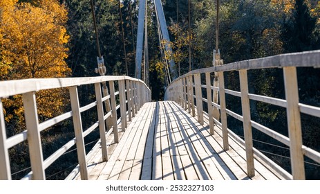 A wooden suspension bridge stretches across a lush forest, framed by vibrant autumn foliage in warm hues, inviting exploration and adventure in nature. - Powered by Shutterstock