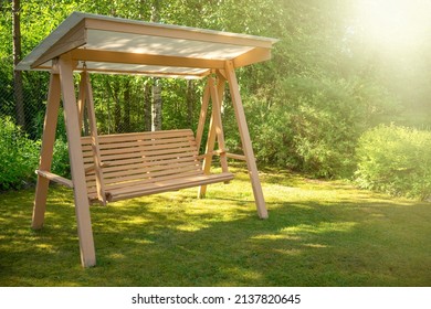 Wooden swing in the green garden. Landscaping of a private plot for recreation. Vacation in the country in summer. Swing for the garden with your own hands.