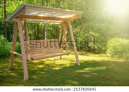Wooden swing in the green garden. Landscaping of a private plot for recreation. Vacation in the country in summer. Swing for the garden with your own hands.