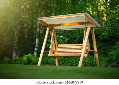 Wooden swing in the green garden. Recreation in the park. Garden design. Relax in the fresh air. Garden furniture made of wood.