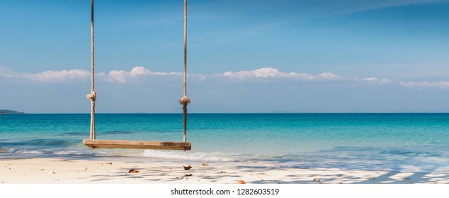 Wooden swing on the beach with tree,sea and blue sky of tropical island banner background and copy space.
